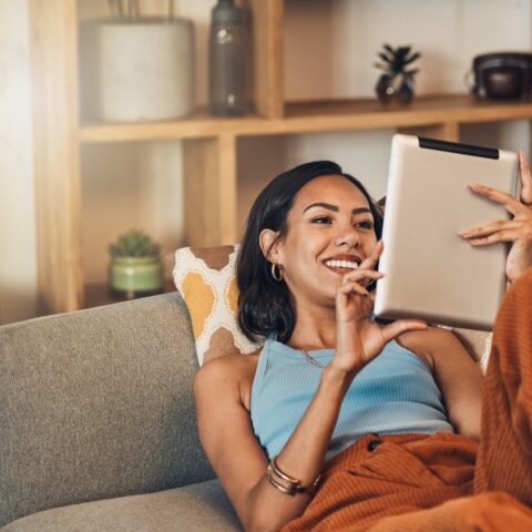 Woman relax on couch with tablet, online streaming with internet and reading ebook or watching film at home. Happy female person with technology, subscription and mobile app with break in living room